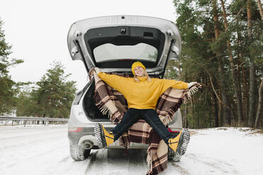 Happy woman with warm clothing sitting in car trunk at winter - SIF00052