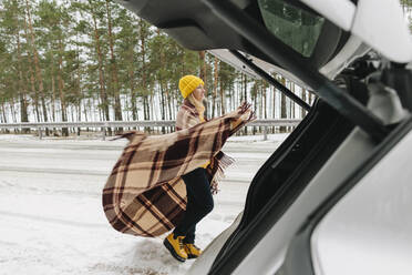 Woman with blanket standing by car in winter - SIF00053