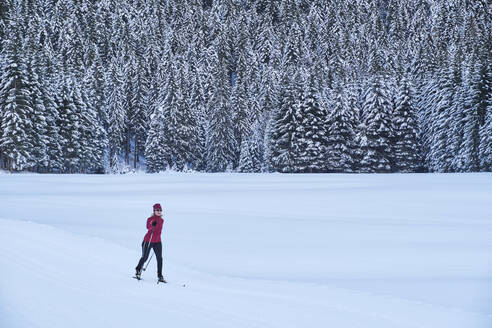 Aktive ältere Frau in Skikleidung beim Skifahren im Winterwald im Urlaub - MRF02510
