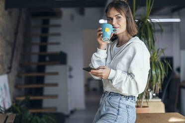 Frau mit Mobiltelefon beim Kaffee trinken zu Hause - JSRF01924