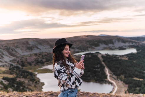 Frau stehend mit Handy in einer Landschaft mit See und Bergen - CAVF95691