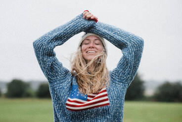 Frau genießt die windige Natur in einem Pullover mit amerikanischer Flagge - CAVF95725