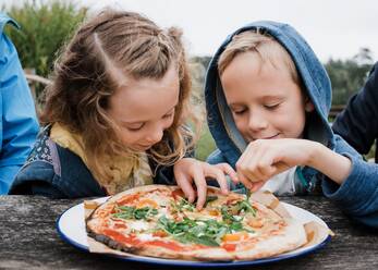 Mädchen und Junge essen gemeinsam Pizza in einem Restaurant im Freien - CAVF95728