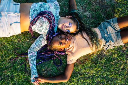 Multirassisches weibliches Paar, das im Gras liegt. Lesbisches Paar - CAVF95736