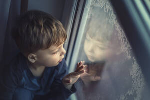Kleiner Junge schaut auf ein gefrorenes Fenster und sieht sein eigenes Spiegelbild - CAVF95749