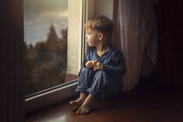 Small boy in blue clothes sitting on the floor by window and loo - CAVF95750