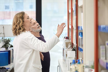 Pharmacist assisting customer taking medicine from shelf in pharmacy store - ZEDF04438