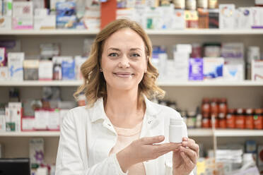 Lächelnde Apothekerin mit Medikamentenflasche in der Apotheke - ZEDF04446