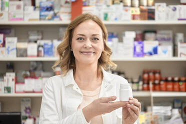 Smiling female pharmacist with bottle of medicine at pharmacy - ZEDF04446