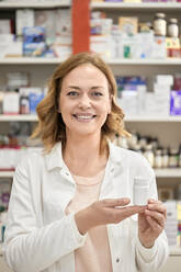 Happy female pharmacist with bottle of medicine at pharmacy store - ZEDF04447