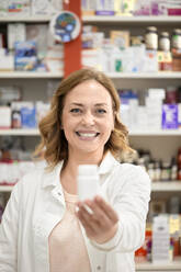 Happy pharmacist giving bottle of medicine standing in pharmacy store - ZEDF04448