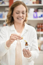 Smiling pharmacist opening bottle of cannabis oil at pharmacy store - ZEDF04461