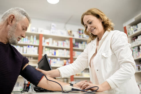 Lächelnde Apothekerin misst den Blutdruck eines Patienten in einer Apotheke - ZEDF04462