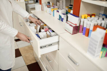 Pharmacist arranging medicines in drawer at pharmacy store - ZEDF04464