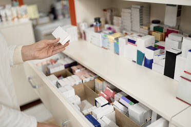 Pharmacist holding box of medicine by drawer at pharmacy store - ZEDF04465