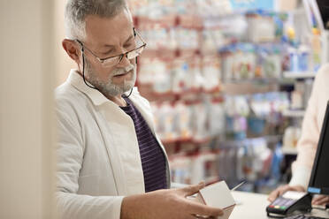 Pharmacist reading instructions on medicine box at pharmacy store - ZEDF04469