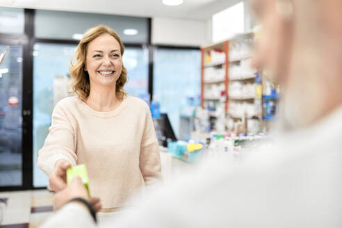 Smiling customer receiving medicine from pharmacist at pharmacy store - ZEDF04476