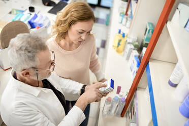 Pharmacist helping customer reading instruction on medicine box at pharmacy store - ZEDF04477