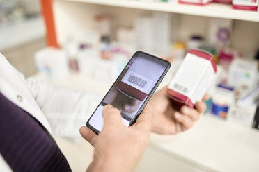 Pharmacist scanning barcode of medicine box through smart phone at pharmacy store - ZEDF04478