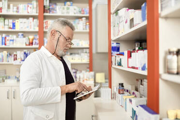 Pharmacist using tablet PC by shelf in pharmacy store - ZEDF04479