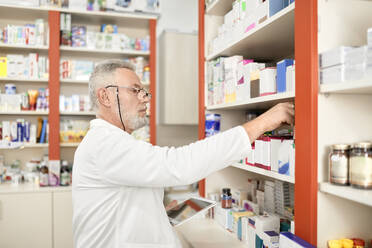 Pharmacist holding tablet PC stacking medicine on shelf at pharmacy store - ZEDF04480