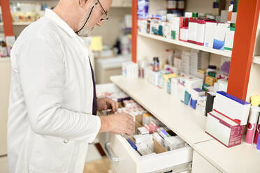 Pharmacist wearing eyeglasses opening drawer of medicines at pharmacy store - ZEDF04483