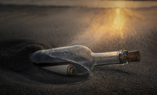 Glass bottle with message inside on beach at sunset - TETF00360