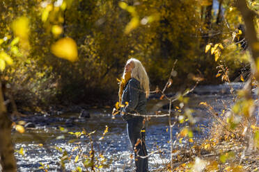 Vereinigte Staaten, Idaho, Sun Valley, Ältere Frau steht im Sonnenlicht am Fluss im Herbst - TETF00371
