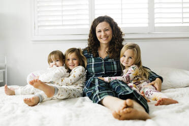 Woman sitting with her daughters on bed - TETF00410