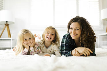 Mother and daughters lying on bed in pajamas - TETF00412