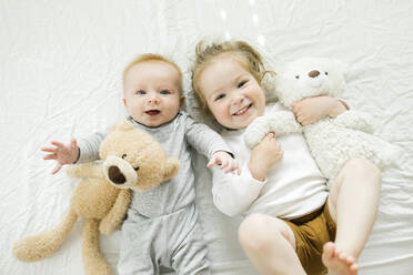Portrait of siblings lying on bed with their teddy bears - TETF00419