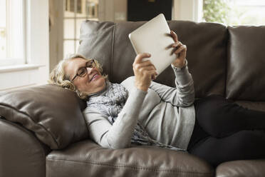 Ältere Frau auf dem Sofa liegend mit Blick auf ein digitales Tablet - TETF00469