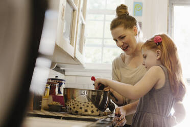 Mid adult mother giving daughter a helping hand in kitchen - TETF00481