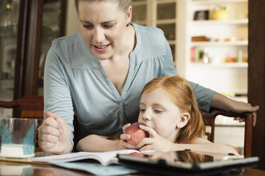 Mid adult mother helping daughter with homework at dining room table - TETF00482