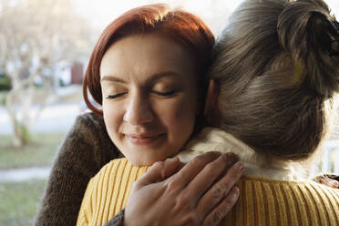 Close up of senior woman and adult daughter hugging on porch - TETF00494