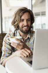 Mittlerer erwachsener Mann in einem Café, trinkt Kaffee, benutzt einen Laptop - TETF00499