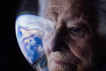 Nahaufnahme einer konzentrierten älteren Frau im Raumanzug, die die Erde betrachtet und über die Zukunft des Globus nachdenkt - ADSF33765