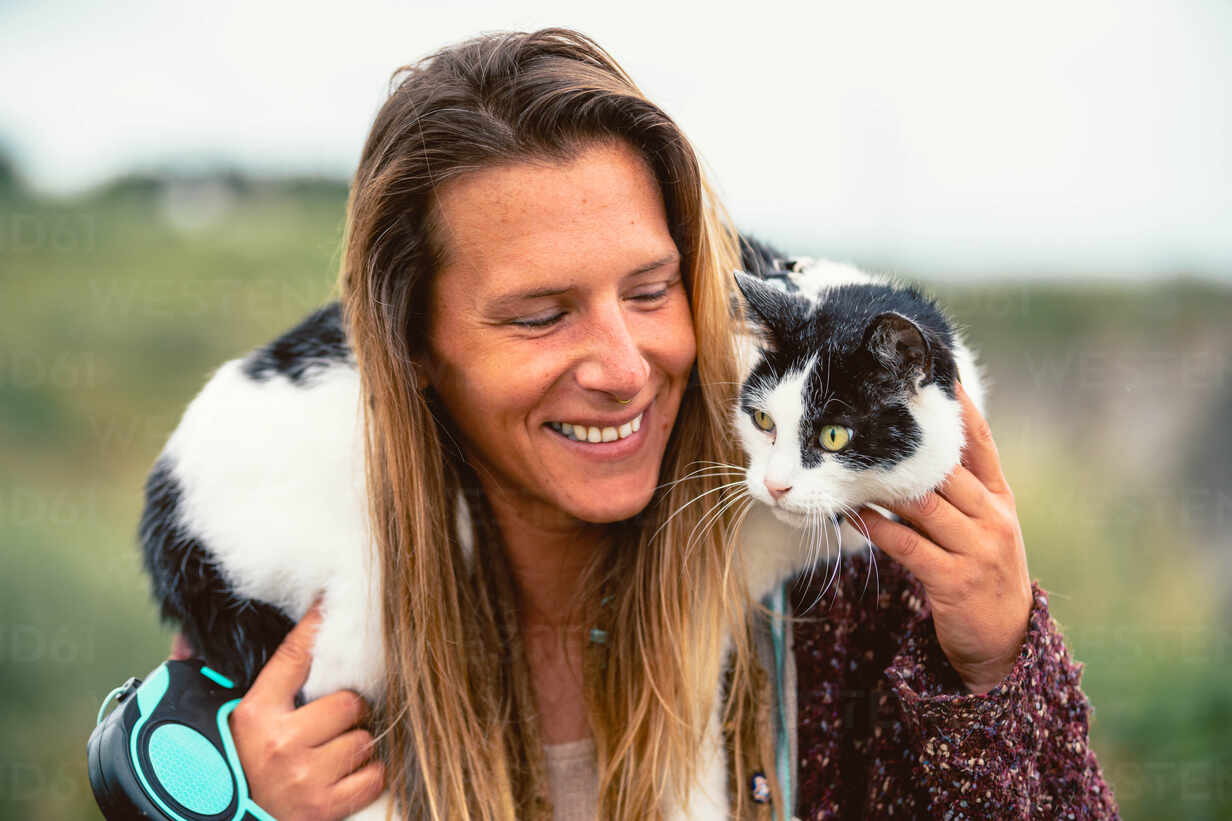 Happy female owner with long hair stroking fluffy domestic cat lying on