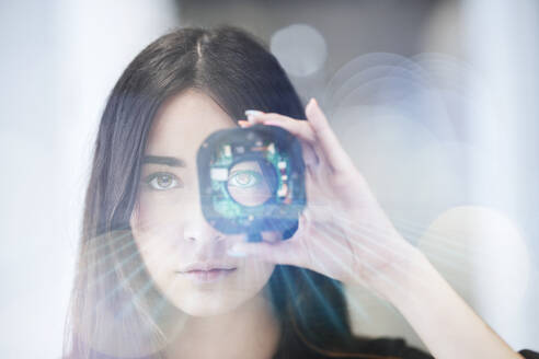 Junge Geschäftsfrau blickt durch ein offenes Kameraobjektiv im Büro - CVF01959
