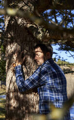 Mann mit geschlossenen Augen umarmt Baum - VEGF05298