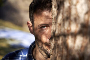 Mann versteckt sich an einem sonnigen Tag hinter einem Baumstamm - VEGF05300