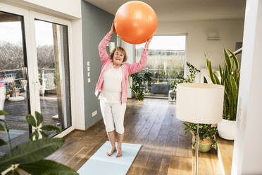 Glückliche ältere Frau, die mit einem Fitnessball zu Hause trainiert - UUF25690