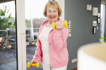 Happy senior woman exercising with dumbbell at home - UUF25695