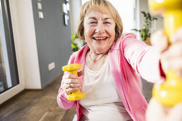 Glückliche ältere Frau, die zu Hause mit gelben Hanteln trainiert - UUF25702