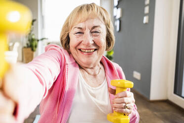 Fröhliche ältere Frau, die zu Hause mit gelben Hanteln trainiert - UUF25703