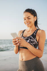 Lächelnde schöne Frau Textnachrichten durch Smartphone am Strand - OYF00702