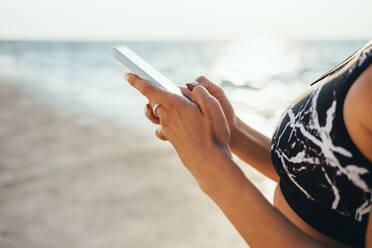 Woman in sports bra using smart phone at beach - OYF00704