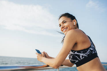 Happy beautiful woman with smart phone standing by railing - OYF00712