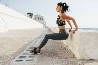 Fit woman exercising by retaining wall on sunny day - OYF00713
