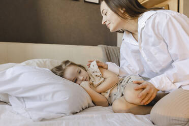 Lächelnde Frau schaut auf ihre Tochter, die zu Hause auf dem Bett liegt - SEAF00623